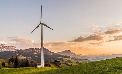 Windrad auf einer Wiese mit Bergen im Hintergrund bei Sonnenuntergang.