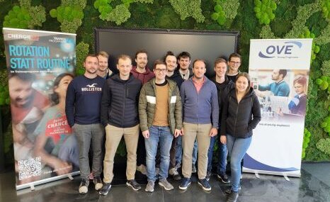 Gruppe von Menschen, die in einem modernen Raum vor einer großen Wand stehen.