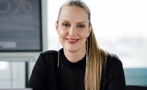 Junge Frau mit langen Haaren und einladendem Lächeln sitzt am Tisch.