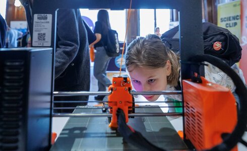 Ein Mädchen beobachtet neugierig einen 3D-Drucker während einer Veranstaltung.