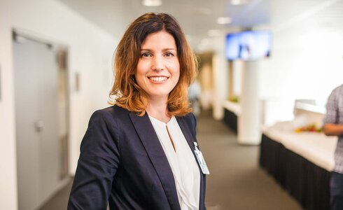 Eine lächelnde Frau in einem Blazer steht in einem modernen Raum.