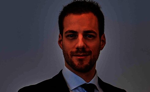 Ein junger Mann in einem Anzug lächelt freundlich in die Kamera.