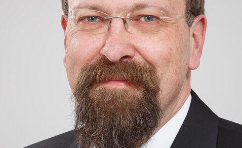 Porträt eines Mannes mit Brille, Bart und Anzug.