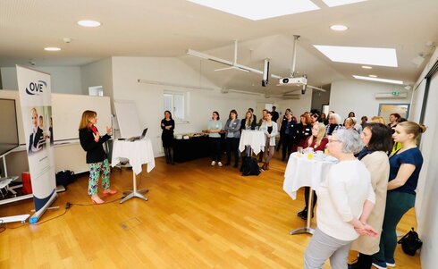 Eine Person spricht vor einer Gruppe von Zuhörern in einem Seminarraum.