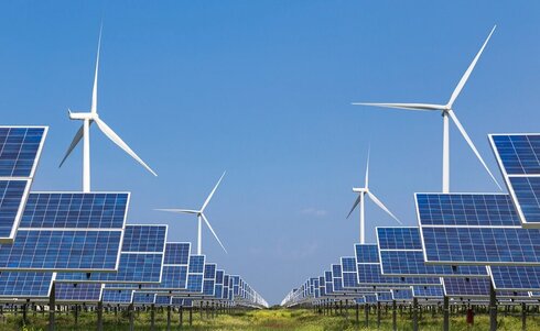 Windkraftanlagen und Solarpanels in einem grünen Feld unter blauem Himmel.