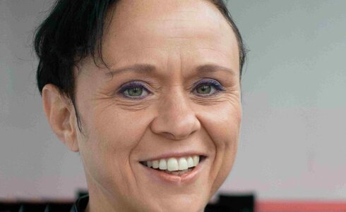 Lächelnde Frau mit schwarzer Lederjacke und kurzer Frisur.