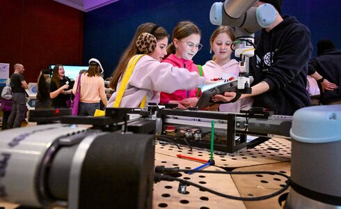 Vier Kinder interagieren mit einem Roboterarm auf einer Technikveranstaltung.