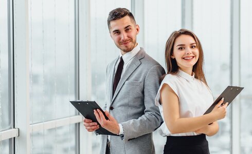 Zwei beruflich gekleidete Personen stehen nebeneinander und halten Notizblöcke in der Hand.