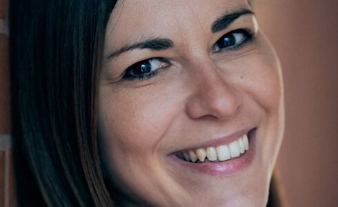 Eine Frau lächelt freundlich vor einer Wand.