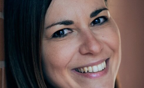 Eine Frau lächelt freundlich vor einer Wand.